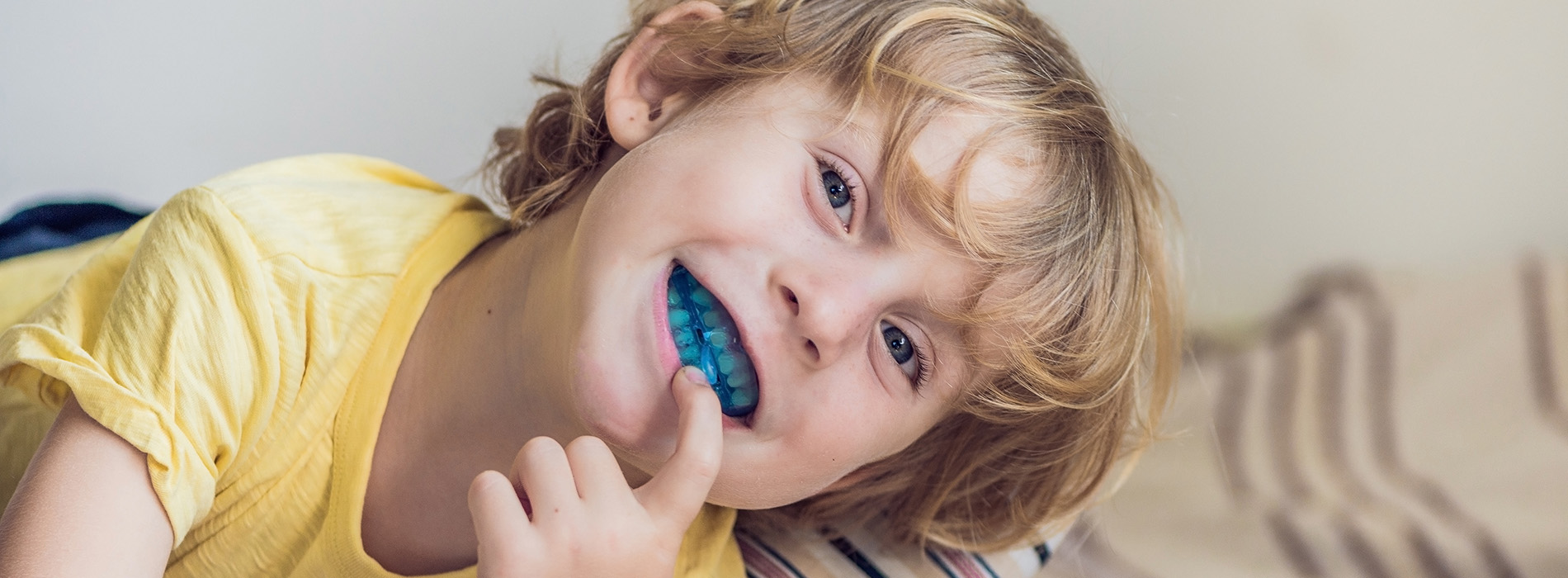The image shows a child with an open mouth, holding a toothbrush, next to a blurred background featuring a person s face.
