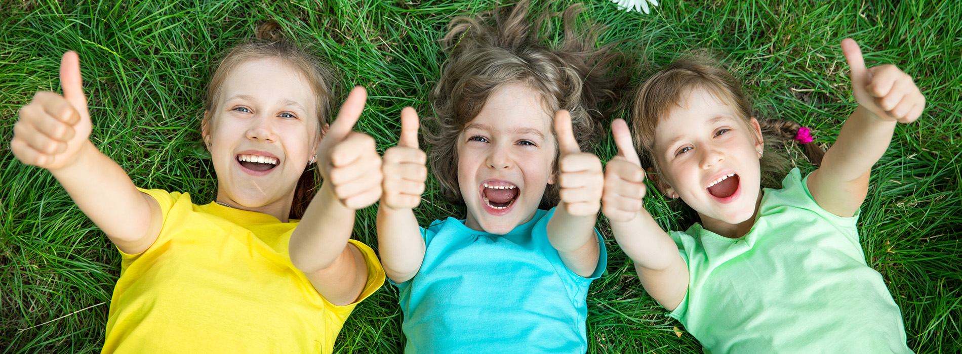 The image shows four children giving thumbs up while sitting on grass.