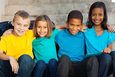 A group of children posing together with smiles, set against a blurred background.