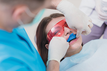 The image depicts a dental professional performing a procedure on a patient with a blue mouthguard, using specialized equipment and tools.