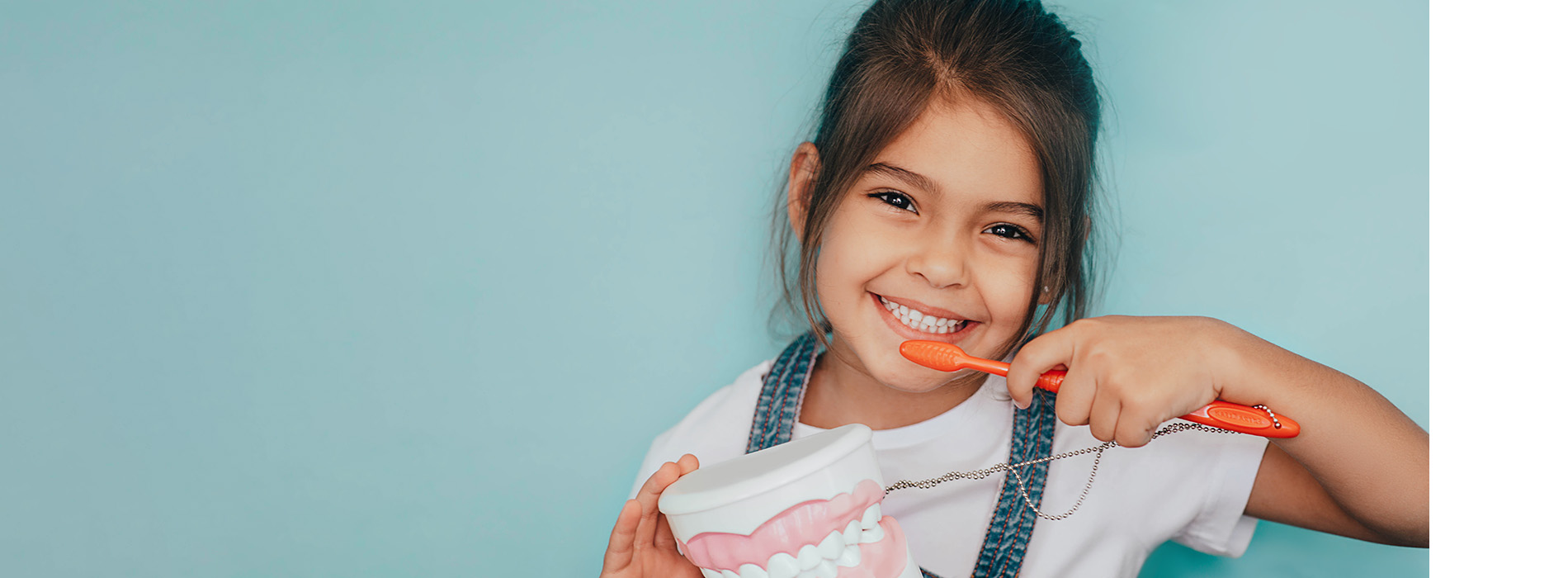 A young girl brushing her teeth with a red toothbrush against a blue background.