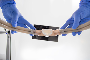 The image shows a person wearing blue gloves handling a flexible tube with a transparent connector attached to it.