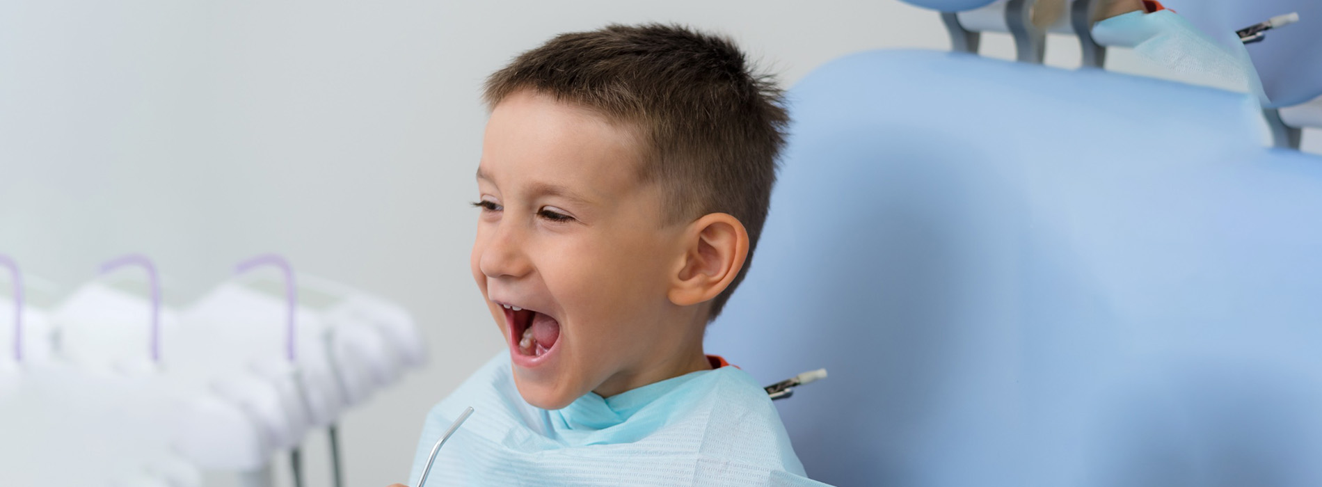 A young boy with a big smile stands next to a dental chair, suggesting a visit to the dentist.